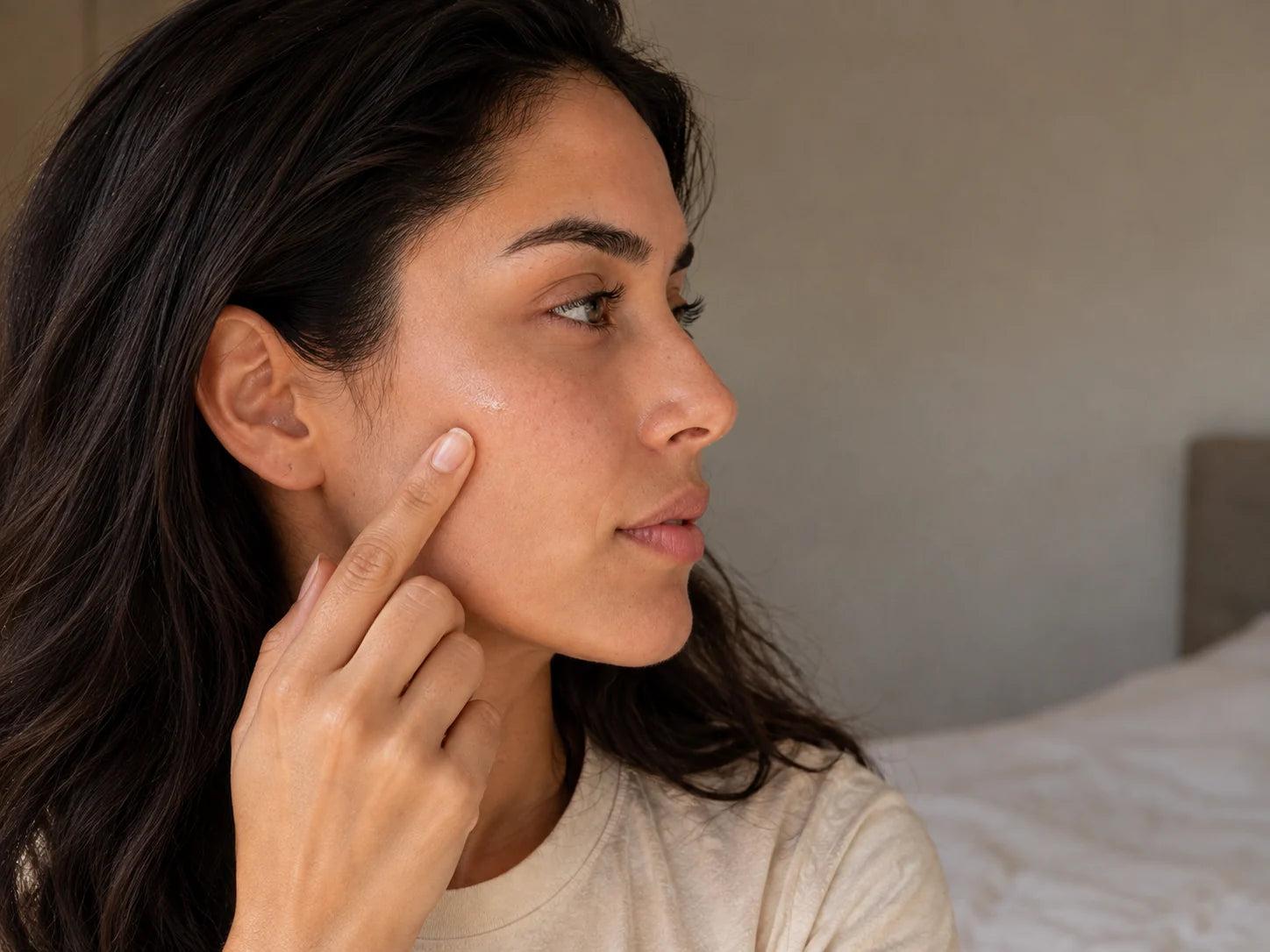 Mujer aplicando sérum transparente en su mejilla durante su rutina de cuidado facial